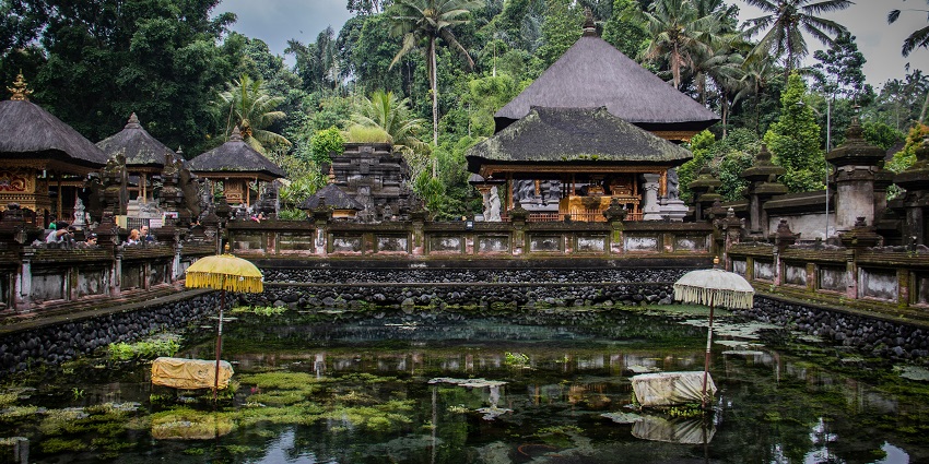 Tirta Empul Temple in Bali surrounded by a water pond and lush greenery on a bright day.