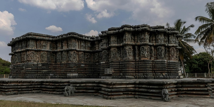 An ancient stone temple with intricate carvings on pillars and walls, under a clear sky.