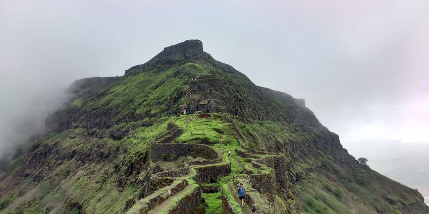 Numerous people are present on the trail to Torna Fort while the weather is cloudy.