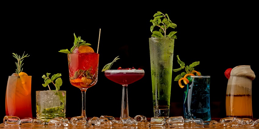A table filled with various drinks, including cocktails, juices, and wine glasses