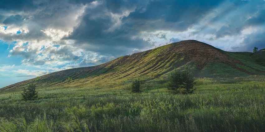 A fantastic view of green hills under a bright, cloudy sky, with sunlight illuminating the grassy slopes.