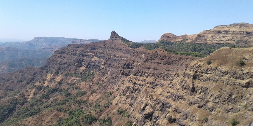Vasota Fort ruins surrounded by dense forest, with mist-covered mountains and calm waters