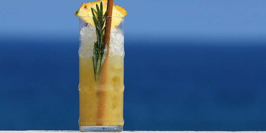 Cocktail in a fancy glass garnished with a piece of pineapple, ice and leaves of mint.