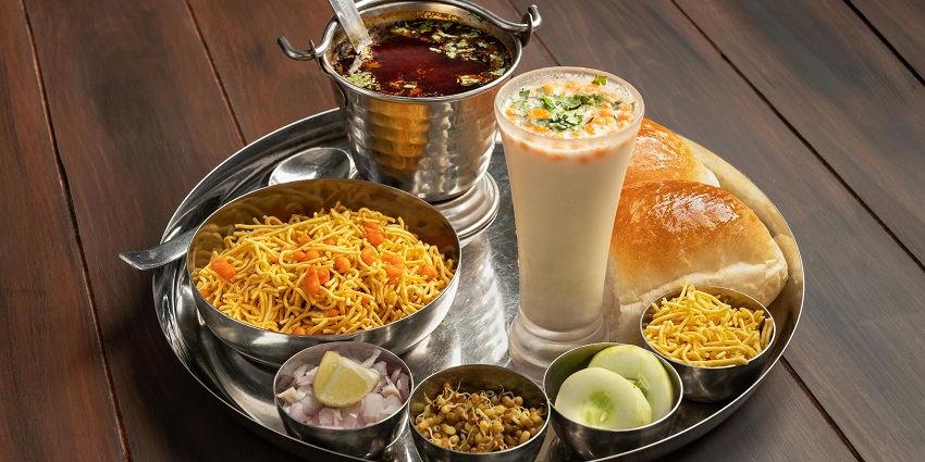 Misal Pav plate featuring soft buns, misal, sev, onion, cucumber, lemon, and buttermilk