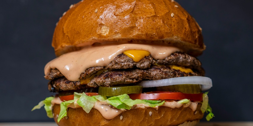 A mouth-watering view of a burger with sliced onions and tomatoes with cheese slice.