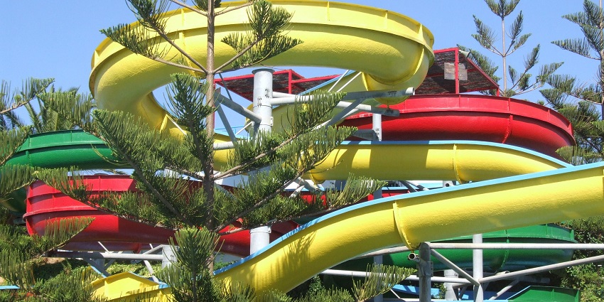 The image of spiral-shaped water slides going down to a pool surrounded by large greenery.