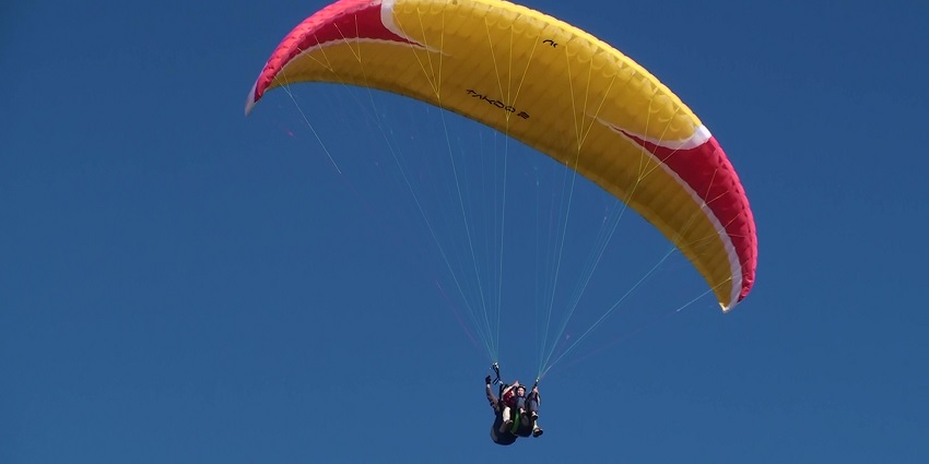 A paraglider glides through the sky, showcasing the beautiful landscapes.