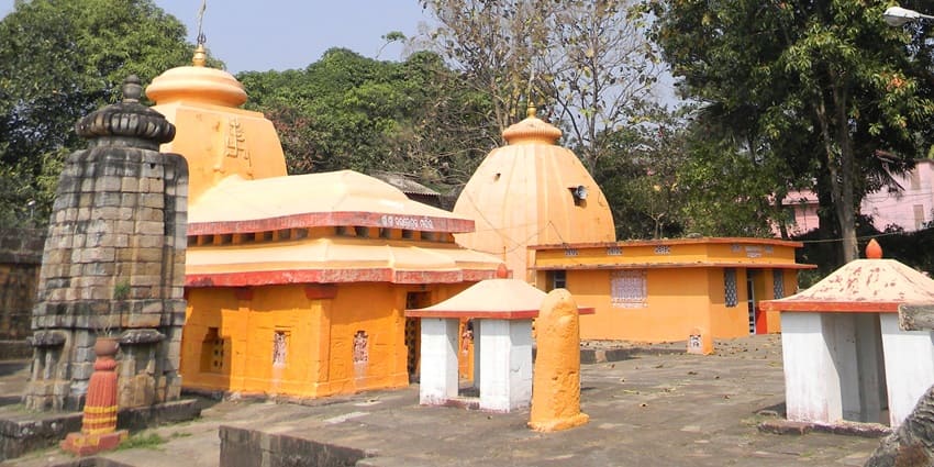 A historic Shiva temple with unique stone walls, nestled in lush greenery.
