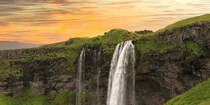 A beautiful waterfall flowing down steep mountains surrounded by greenery.
