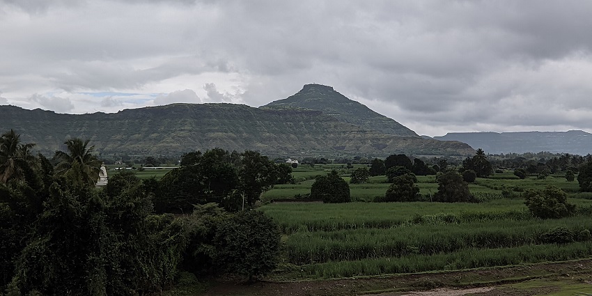 Hilltop fort ruins rise above green fields and scattered trees under a clear blue sky