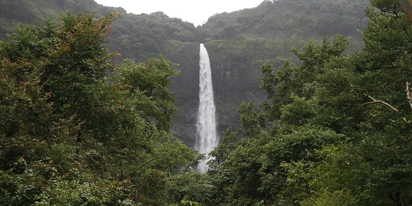 A picture of a majestic waterfall, cascading down a lush green terrain in Satara