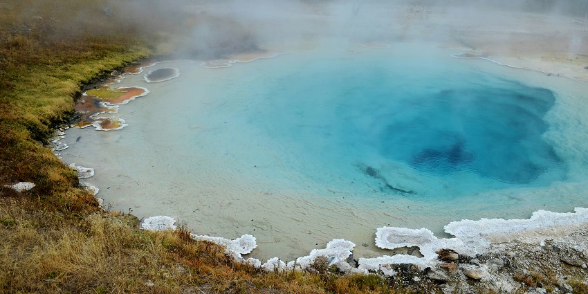 An image of steam rising from a rocky ravine, surrounded by misty natural landscape.