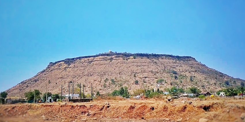 Vardhangad hill fort with stone walls and gate rising against a bright sky.