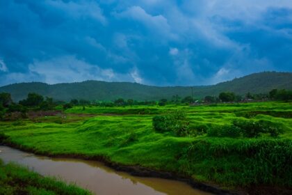 A breathtaking vista of green fields, a tranquil stream and cloudy skies of Maharashta.