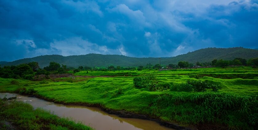 A breathtaking vista of green fields, a tranquil stream and cloudy skies of Maharashta.