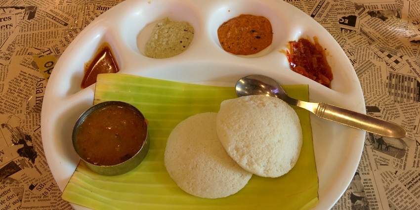A plate of idli served with coconut chutney, tomato chutney and sambhar