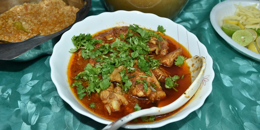 Image of chicken curry served on a white container with yellow rice on the side and lemon