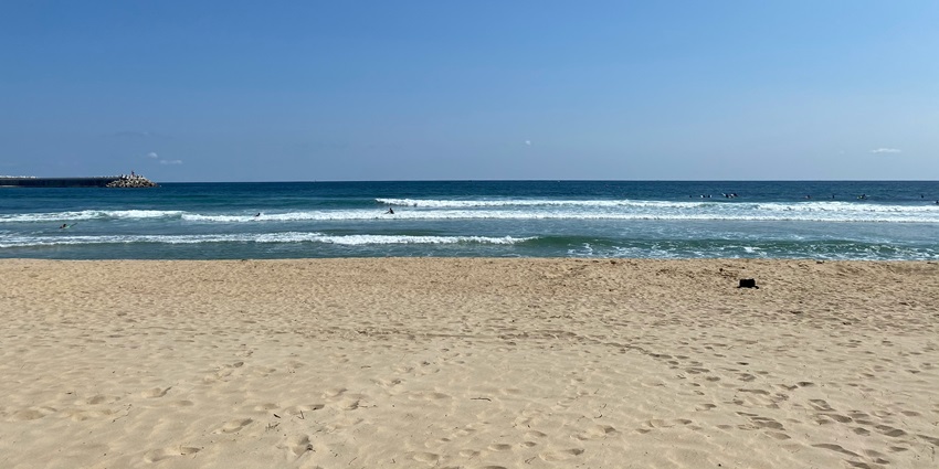 Image of a beach near the shoreline surrounded by clear blue water and under clear blue sky