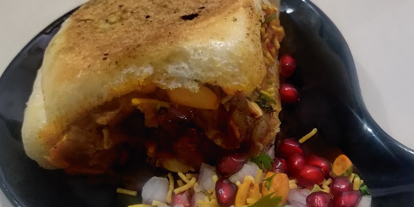 Dabeli, featuring buns filled with potato mixture accompanied by pomegranate seeds and sev
