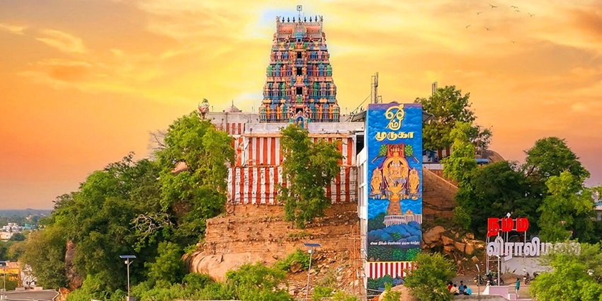 Hilltop Viralimalai Murugan temple with a white façade and green dome, surrounded by lush greenery.