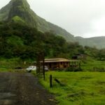 View of Visapur Fort on a hilltop surrounded by greenery under a cloudy sky in Maharashtra.