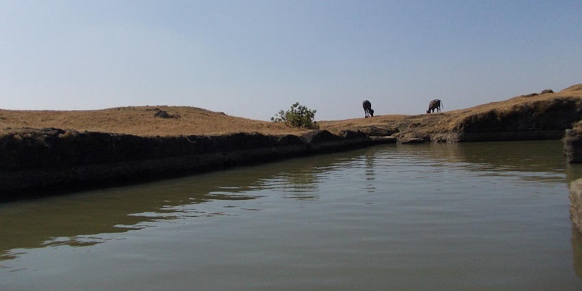 Ancient water tank atop Visapur Fort in Pune, surrounded by stone walls and greenery.