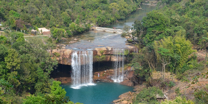 Image of a waterfall cascading through rocks in lush greenery forest during day time view