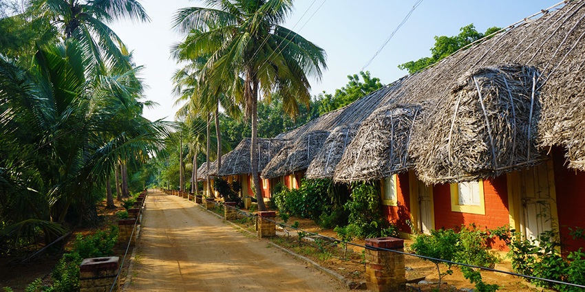 Traditional Indian ashram courtyard with rustic huts and peaceful shaded pathways