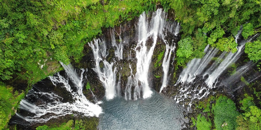 Water is falling from a giant waterfall made of many yet smaller falls covered in green