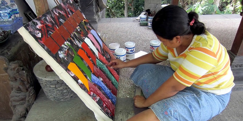 A woman painter in Ubud art gallery markets painting beautiful colour-coordinated art.