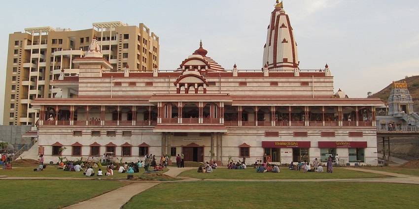 The magnificent architecture of the ISKCON Temple, surrounded by devotees and greenery.