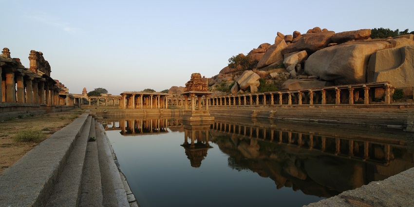 A picture of a pond in a temple with the traditionally architecture of the temple visible in the background