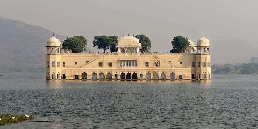 The serene Jal Mahal, a grand structure in a lake, glows under the warm hues of a picturesque sunset.