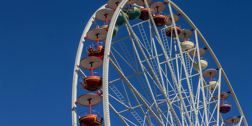 A brightly lit observation wheel in a modern amusement park at night, with colourful lights