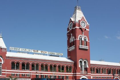 Chennai train station with people waiting on the platform and trains on the tracks.