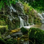 A stunning view of water cascading down rocky cliffs into a pool surrounded by greenery.