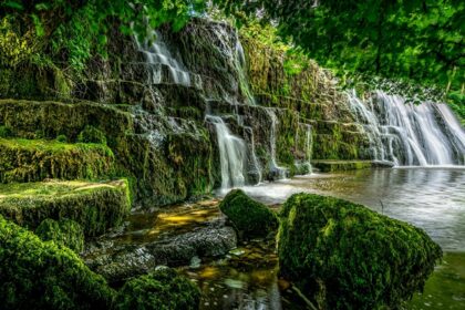 A stunning view of water cascading down rocky cliffs into a pool surrounded by greenery.