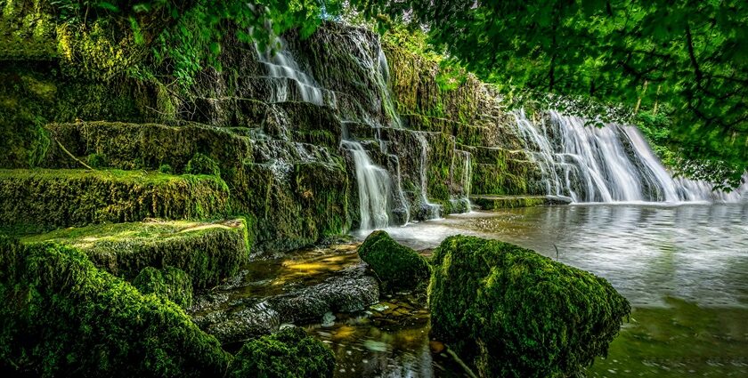 A stunning view of water cascading down rocky cliffs into a pool surrounded by greenery.