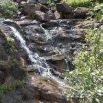 A scenic view along Tamhini Ghat featuring lush green mountains and winding roads.