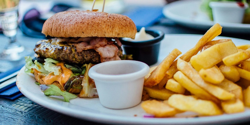 Image of delectable burger filled with non veg and fries on the side served on a plate