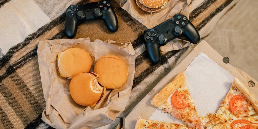 Pizza and hamburgers accompanied by PlayStation controllers, perfect for a gaming night.