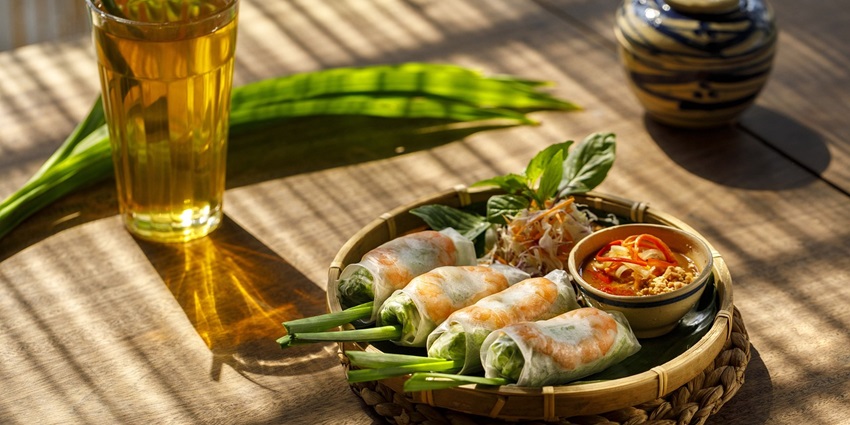An image shows spring rolls served on a white plate, filled with vegetables and herbs at a cafe in Dreamland Beach.