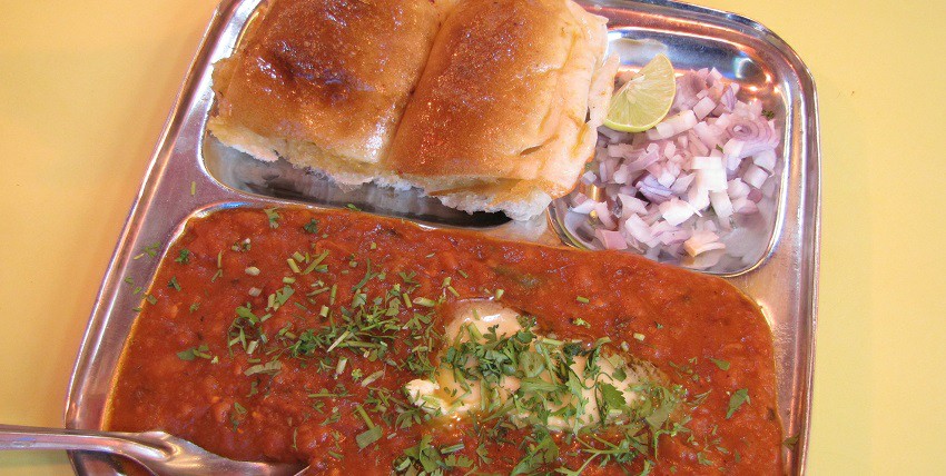 A plate of pav bhaji, served with lemons and onions at a local eatery nearby