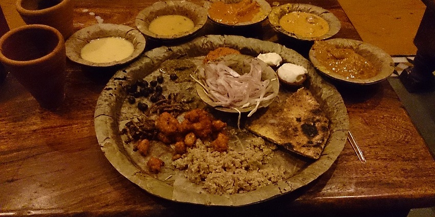 A Rajasthani thali with several dishes and accompaniment is placed on a wooden table.