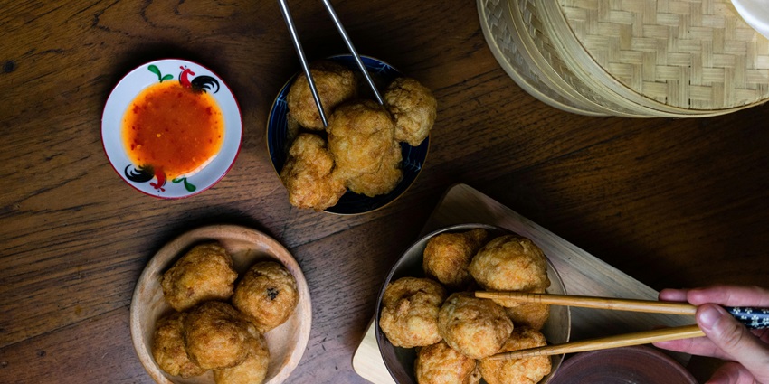 An image showing fried Indonesian meatballs served with a dipping sauce and chopsticks