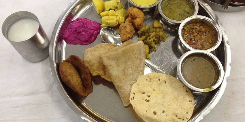 A vibrant Maharashtrian thali featuring various traditional dishes, served on a stainless steel plate