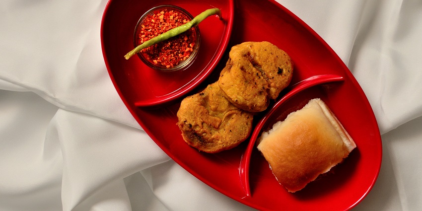 Image of a vada pav served on a red plate in a restaurant Maharashtra