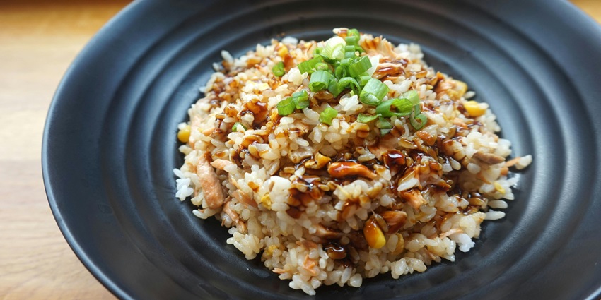 An image of cooked rice served on a black ceramic plate, garnished with green herbs.