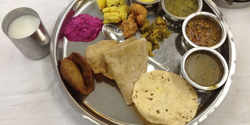 A traditional Maharashtrian thali featuring various dishes served on a round metal plate.