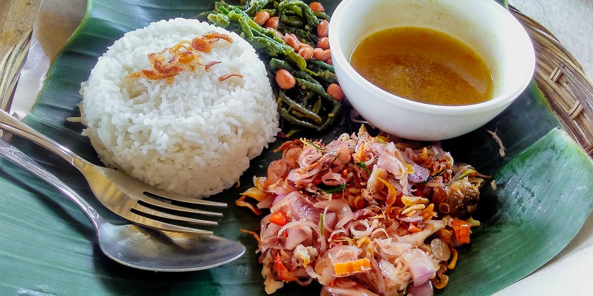 An authentic Balinese dish is served on a green banana leaf with a fork and a spoon